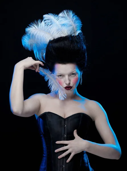 brunette woman with feathers in high hair and corset in old style on a black background