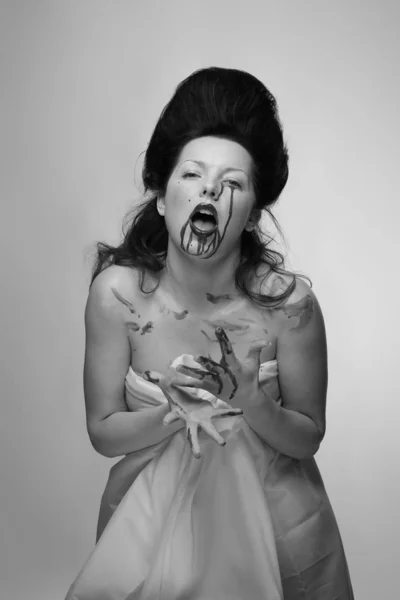 emotional actress brunette woman with pale skin in the role of vampire victims with blood on face, black and white photo in studio