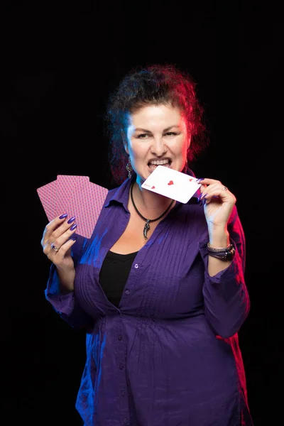 woman in purple clothes holds a deck of cards and shows tricks in a scenic light.