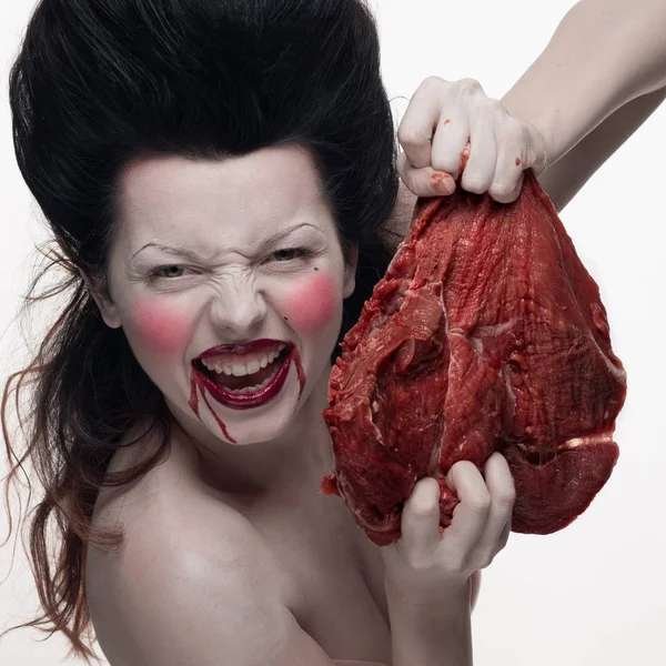 emotional brunette actress in the role of vampire with blood drops on face and a piece of bloody meat.