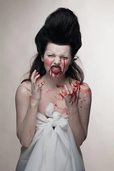 emotional actress brunette woman with pale skin in the role of vampire victims with blood on face on a white background in studio