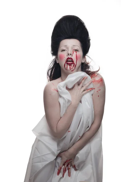 emotional actress brunette woman with pale skin in the role of vampire victims with blood on face on a white background in studio