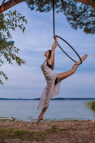 Girl performing acrobatic elements on the ring on the shore of the lake. Training aerial gymnastics
