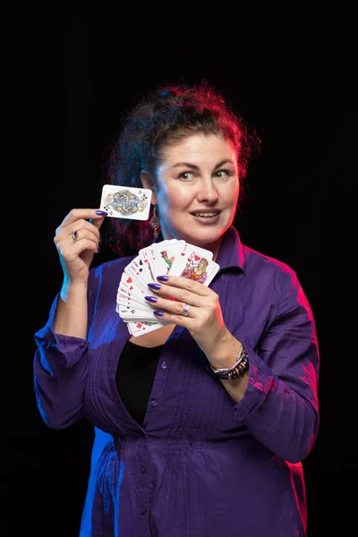 woman in purple clothes holds a deck of cards and shows tricks in a scenic light.