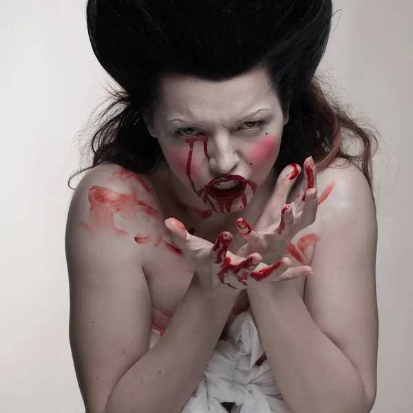 emotional actress brunette woman with pale skin as a vampire with blood on her face on a white background in studio