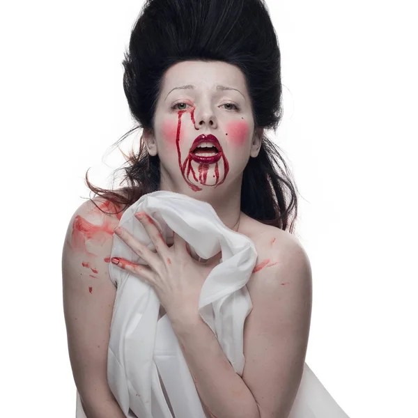 emotional actress brunette woman with pale skin as a vampire with blood on her face on a white background in studio