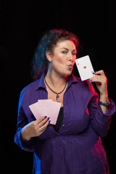 woman in purple clothes holds a deck of cards and shows tricks in a scenic light.