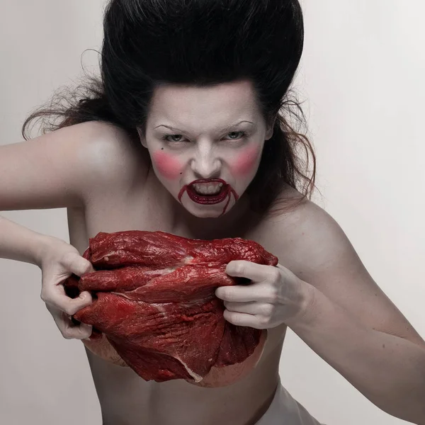 emotional brunette actress in the role of vampire with blood drops on face and a piece of bloody meat.