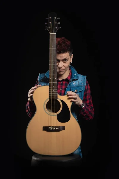 Woman musician with red hair in a denim suit with a guitar on a black background