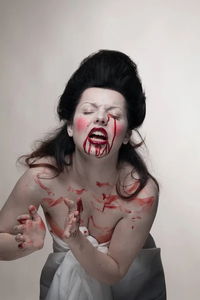 emotional actress brunette woman with pale skin in the role of vampire victims with blood on face on a white background in studio