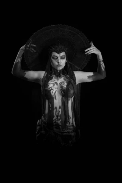 Actress woman in black headdress, body painting, golden figure on body and face, posing on black background