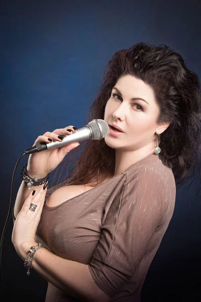 Emotional woman singer with microphone in hands singing and posing against blue background