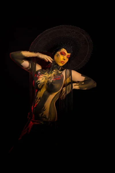 Actress woman in black headdress, body painting, golden figure on body and face, posing on black background