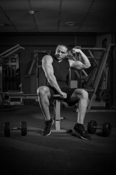 Young male athlete bodybuilder posing and doing sports exercises in the gym