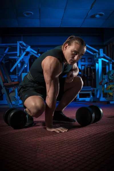 Young male athlete bodybuilder posing and doing sports exercises in the gym