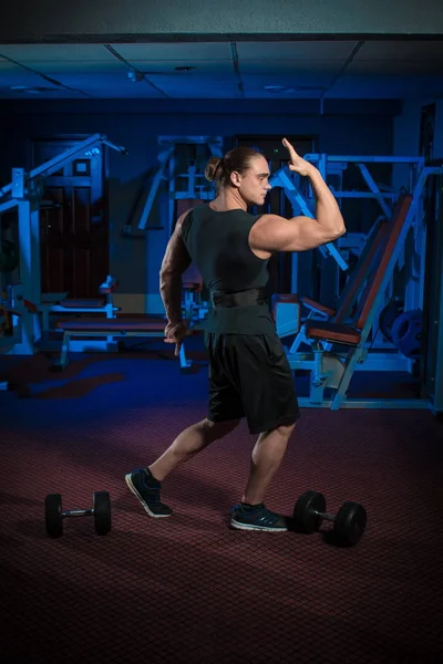 Young male athlete bodybuilder posing and doing sports exercises in the gym