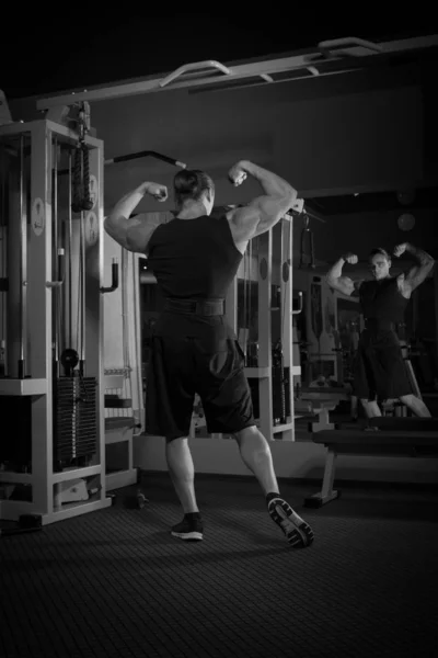 Young male athlete bodybuilder posing and doing sports exercises in the gym