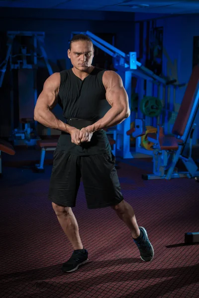 Young male athlete bodybuilder posing and doing sports exercises in the gym