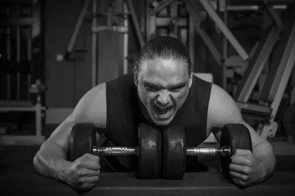 Young male athlete bodybuilder posing and doing sports exercises in the gym