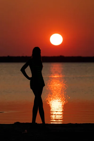 female silhouette at river shore on dramatic sunset background