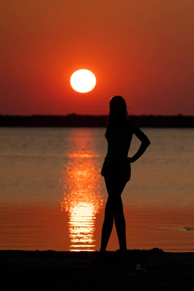 female silhouette at river shore on dramatic sunset background