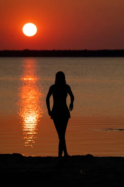 female silhouette at river shore on dramatic sunset background