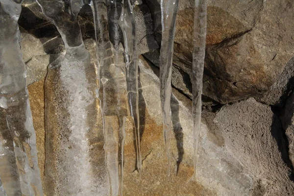 Icicles hanging on a ledge with rocky bacground — Stock Photo, Image