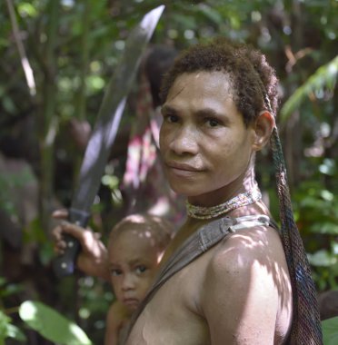 WILD JUNGLE, IRIAN JAYA, NEW GUINEA, INDONESIA - MAY 19, 2016: Portait of Papuan woman and little boy of the Nomadic Forest Tribe Korowai. Jungle of New Guinea Island. clipart