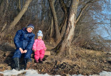 Genç Anne ve orman içinde erken bahar döneminde oturan küçük kız