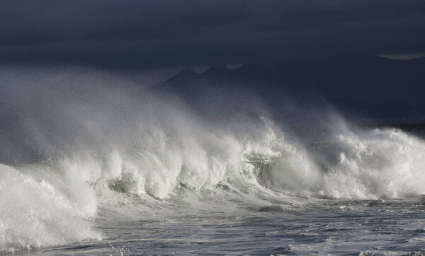 Seascape. Powerful ocean wave on the surface of the ocean. Wave breaks on a shallow bank. Stormy weather, stormy clouds sky background.
