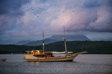 Günbatımında okyanusta geleneksel Endonezya gemisi. Okyanus ve dağlar manzaralı. Komodo Adası. Moluccas, Endonezya Maluku, Baharat Adaları, Endonezya