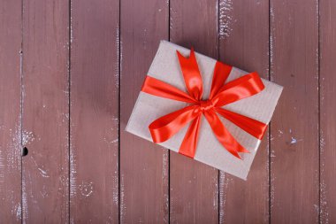 Kahverengi ahşap arka plan üzerinde kırmızı yay yukarıdan tarafından küçük paket teslim hizmeti - postalama ve paketleme bağladı.