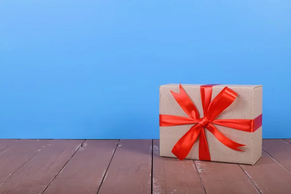 Postage and packing delivery service - small Package tied up by a red bow on a brown wood and blue wall background.
