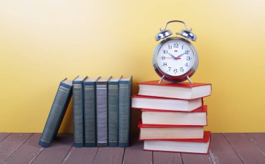 Bilim ve eğitim - çalar saat ve ahşap masa ve sarı zemin üzerine Derma kitabın kazık grubu.