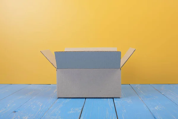 梱包サービス 青の木と黄色の壁の背景にオープン パッケージ正面 — ストック写真