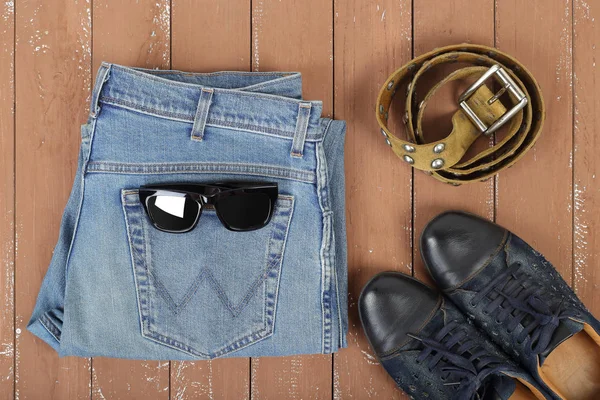 Clothes, shoes and accessories - Top view sunglasses, leather belt, shoes and blue jeans on a wooden background