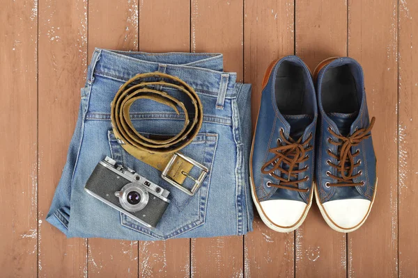 Clothes, shoes and accessories - Top view old camera, leather belt, gumshoes and blue jeans on a wooden background