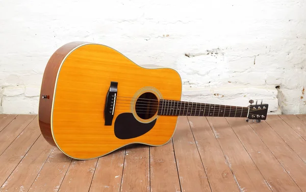 Musical instrument - Classic acoustic guitar on a brick background and wooden floor.
