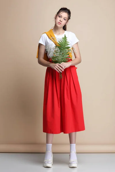 Hermosa chica en ropa varicolor con la cesta de flores sobre un fondo beige Imagen De Stock