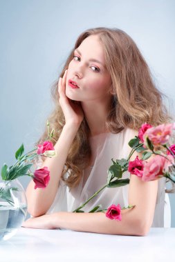 Güzel kız, mavi arka planda izole edilmiş çiçekler, duygular, kozmetik