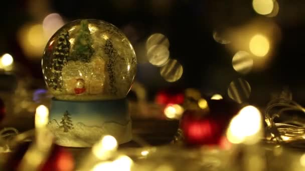 Bola de nieve de Navidad Copo de nieve con nevadas en mesa de madera con luces de Navidad y decoraciones en el fondo del árbol de Navidad — Vídeos de Stock