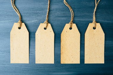 Kahverengi ahşap arka planda dört tane boş karton etiket. Ahşap zemin üzerinde ip olan dört boş etiket..