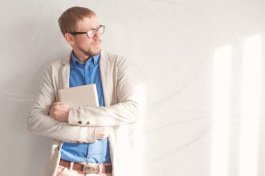 Genç işadamı pencere ve duvarın yanında duruyor ve tablet bilgisayar kullanıyor..