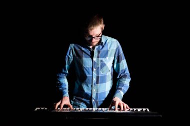 Ekose gömlekli klavyeci koyu arkaplanda çalıyor..