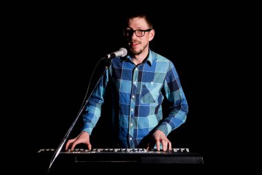 Ekose gömlekli klavyeci koyu arkaplanda çalıp şarkı söylüyor..