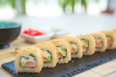 Sıcak suşi rulosu suşi siyah tahtada yuvarlanıyor. Japon yemeği..
