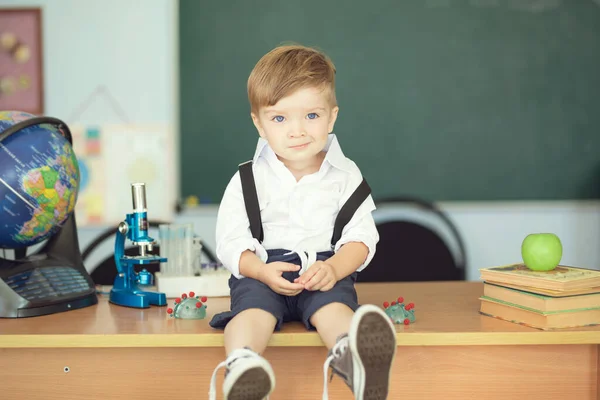 귀엽고 귀여운 소년이 책상에 앉아서 배경에 교실에서 있습니다 — 스톡 사진