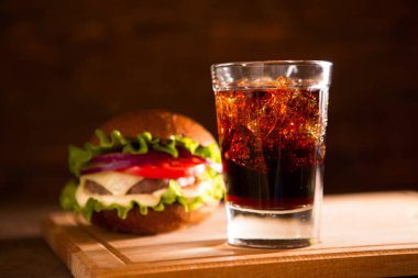 Tahta masa üzerinde taze büyük hamburger ve cam kola fast food konsepti.