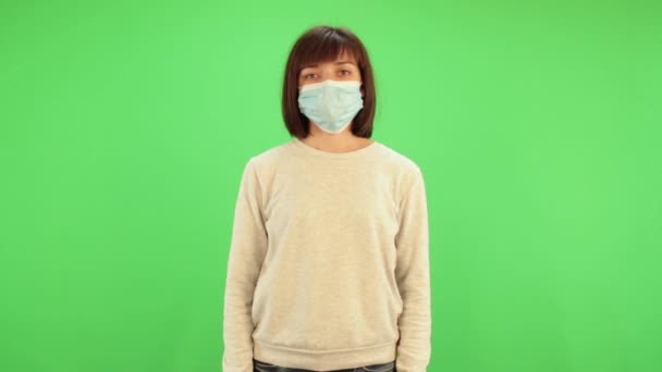 Een vrouw zet een medisch masker op een chromakey. Virusbeschermingsgel, ontsmettingsmiddel. Voorkomen van verspreiding van coronavirus covid-19. — Stockvideo