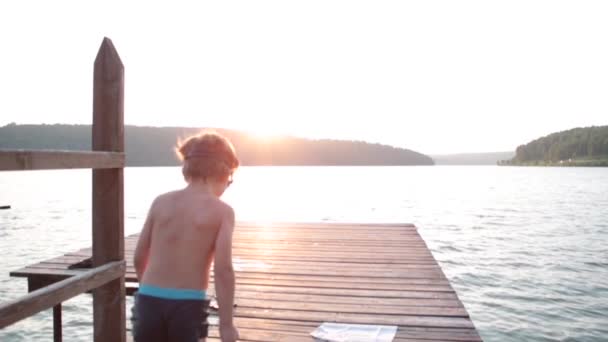 Güneşli bir yaz gününde bir çocuk iskeleden denize ya da dağlarda göle atlıyor.. — Stok video